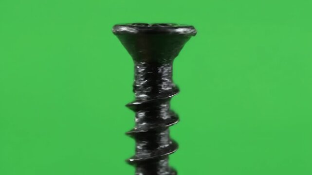Macro video of a spinning black steel drywall screw isolated on a vibrant green screen background