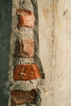 Close-up of an exposed red brick wall partially covered with aged plaster, showcasing rustic textures, weathered construction materials, and vintage architectural details. The image highlights the con