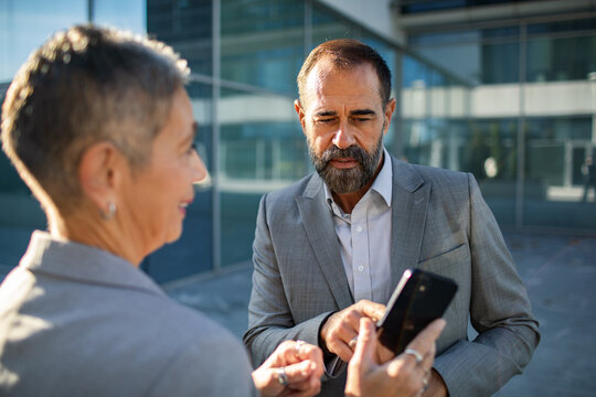 Senior business colleagues reviewing smartphone outside office