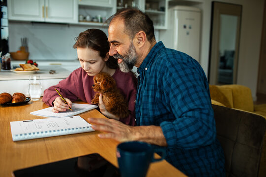 Father helping daughter with homework at kitchen table with puppy