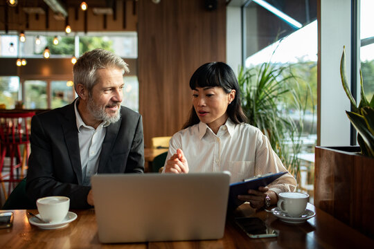 Two business colleagues collaborating with laptop at coffee shop