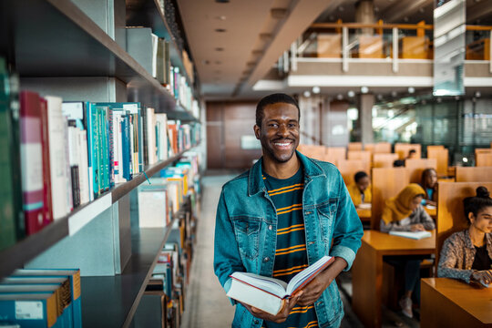 Smiling student holding book in university library