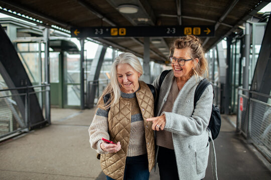 Two senior women using smartphone at train station
