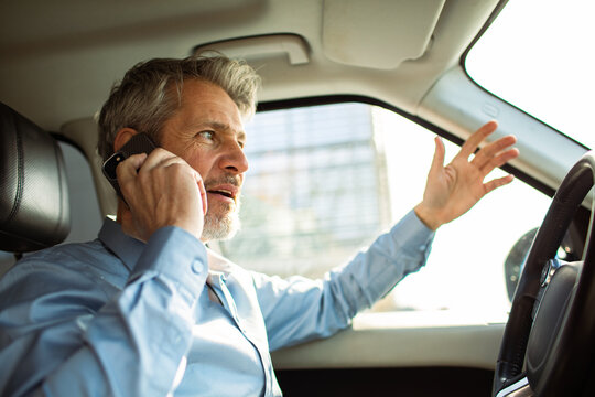 Middle-aged businessman talking on phone while driving in car