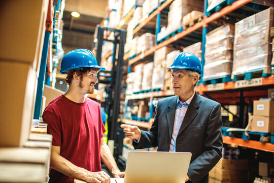 Warehouse manager and worker reviewing inventory on laptop in distribution center