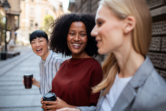 Three diverse women laughing with coffee on city street