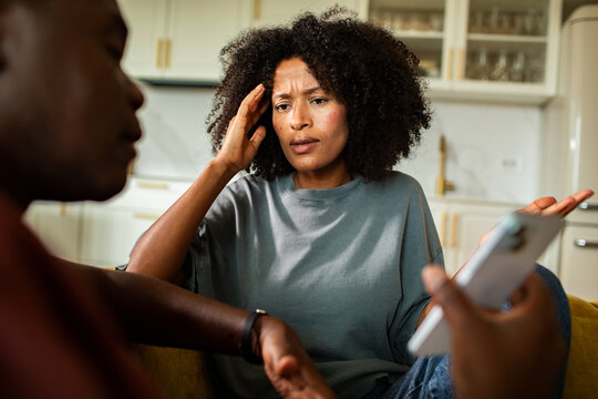 Concerned woman confronting partner about phone at home kitchen