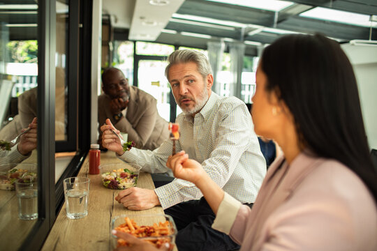 Coworkers eating lunch and talking in modern office cafeteria