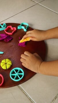 Vertical child hands cutting purple playdough with plastic tool