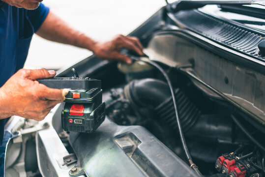 Auto repair technician checking vehicle motor with LED flashlight, authentic photo, not AI.