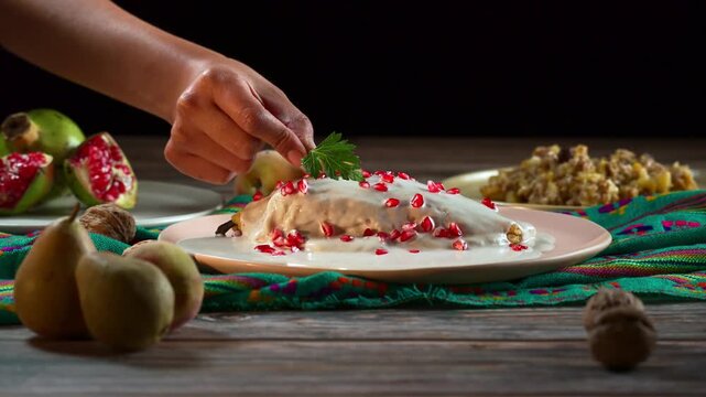 Woman's hand garnishing traditional Mexican Chile en Nogada with fresh parsley leaf on wooden table