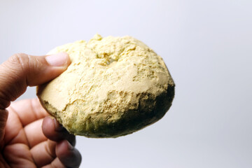 Naklejka premium hand holding a round green matcha pastry coated with a fine, powdery yellow dusting against a clean white background.