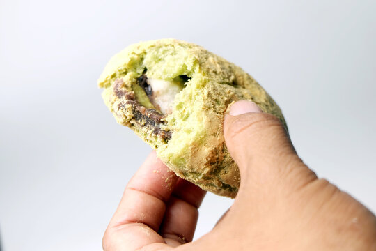 person holding a partially eaten or torn open matcha bread, revealing a sweet filling inside the soft, powder-dusted green bun.