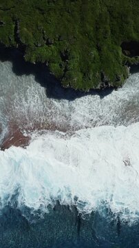 Aerial view of powerful ocean waves crashing against the rugged green coastline of Niue in the South Pacific.