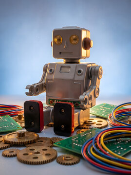 Small humanoid toy robot with scattered gears, circuit boards and wires on blue background