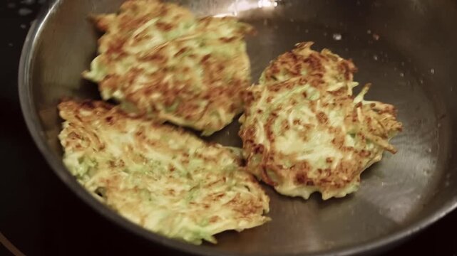 Roasting dish. Vegetarian meal. Preparing tasty vegetable fritter in oil steel pan. Cooking zucchini potato pancakes tossing process.