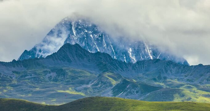 Time-lapse landscape of Yala Snow Mountain Sichuan China, herd of yaks grazing on alpine grassland, cloudy sky over snow-capped peaks and highland meadow