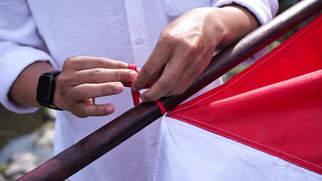 A man tie the Indonesian red and white flag to a pole at Tukad Unda waterfall in Klungkung, Bali, preparing the national flag for a cultural performance and celebration.