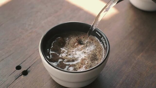 Barista pouring hot water into a cupping bowl for coffee quality testing and sensory analysis.