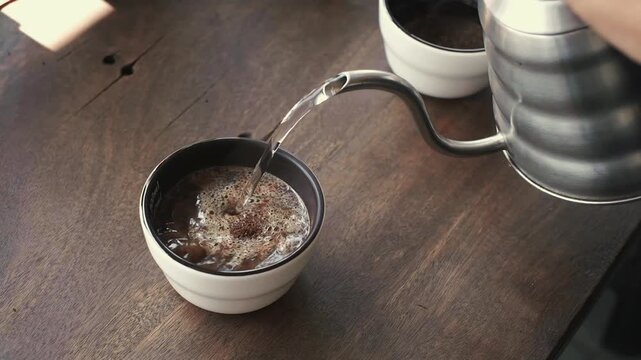 Barista pouring hot water into a cupping bowl for coffee quality testing and sensory analysis.