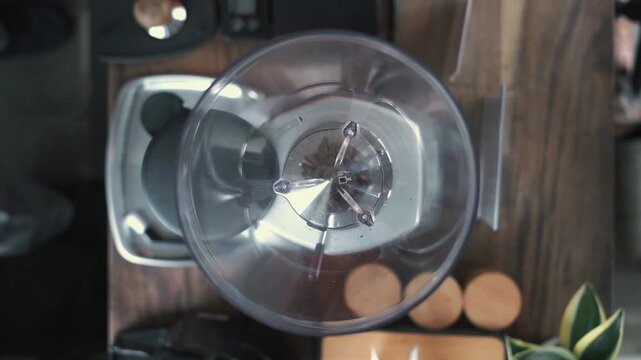 Top view of roasted coffee beans being poured into an electric grinder hopper from a metal scoop.
