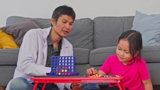 Child psychologist in white coat guiding young girl patient through an educational game on small table