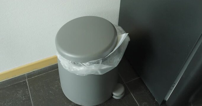 Person throwing a sheet of paper into a trash bin, representing document disposal, office cleanup, and waste management.