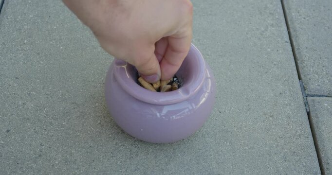Person extinguishing a cigarette in an overflowing ashtray, illustrating chain smoking, nicotine addiction, and heavy tobacco use.
