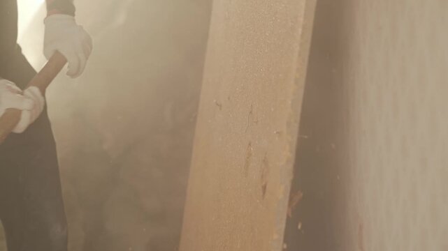 Slow motion, man striking interior wall with sledgehammer during demolition