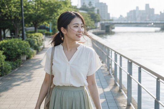 川沿いの遊歩道を歩く白いブラウスの笑顔の女性