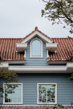 Blue house facade featuring a dormer window, terracotta tile roof, and two lower windows with white frames.