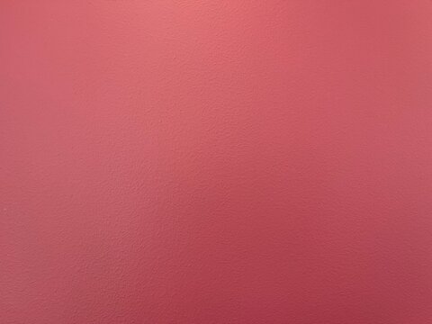Textured dark pink wall background with soft overhead lighting gradien. Plain dusty rose painted concrete surface texture for backdrop. Minimalist coral pink plaster wall background with subtle grain.