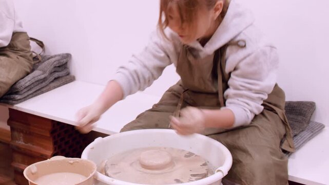 Artistic education. Handmade art. Inspired kids learning hobby sculpting clay using ceramic craft wheel in artisan pottery workshop.