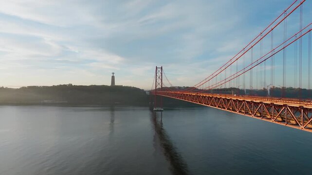 25 de Abril Bridge and Cristo Rei at sunrise in Lisbon Portugal, drone dolly along glowing support beams