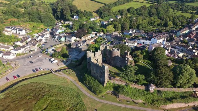 Aerial drone footage of the historic village of Laugharne in Carmarthenshire, Wales, featuring the River Coran estuary, traditional buildings, surrounding countryside and picturesque rural landscape 