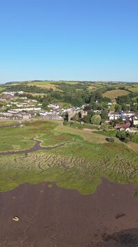Aerial drone footage of the historic village of Laugharne in Carmarthenshire, Wales, featuring the River Coran estuary, traditional buildings, surrounding countryside and picturesque rural landscape 