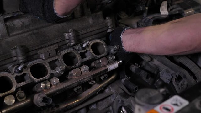 A close-up of a mechanic disassembling an engine under the hood of a car in a service station. An unrecognized mechanic repairing an engine. A man using tools for his work.