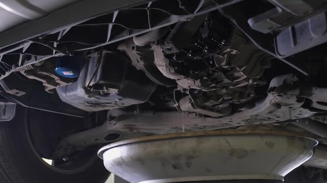 A close-up of a mechanic blowing air through the engine after changing the oil under the car. The mechanic is purging the bottom of the machine after replacing the engine oil.