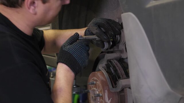 A detailed view of a mechanic working on a vehicle, focusing on the repair of a wheel, brake pads, silent blocks, and shock absorbers at a repair facility.