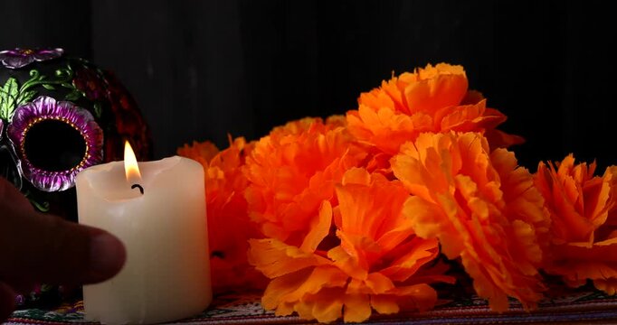 Cinematic horizontal camera pan over traditional Mexican Dia de los Muertos altar with painted black metallic skull and bright orange flowers.