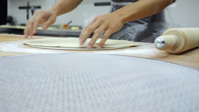 A detailed view of the chef preparing the pizza dough and placing it on a circular baking sheet. The act of making pizza in the restaurant kitchen.