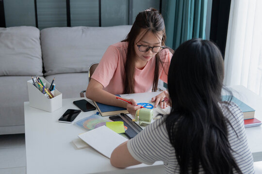 Two Asian girl with books on table doing homework together at home