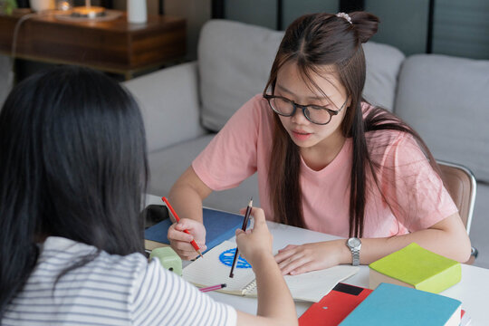 Two Asian girl with books on table doing homework together at home