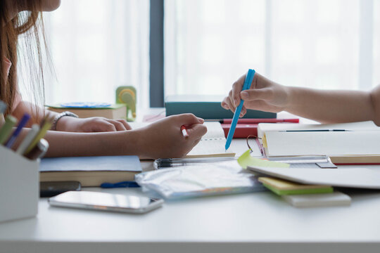Two Asian girl with books on table doing homework together at home