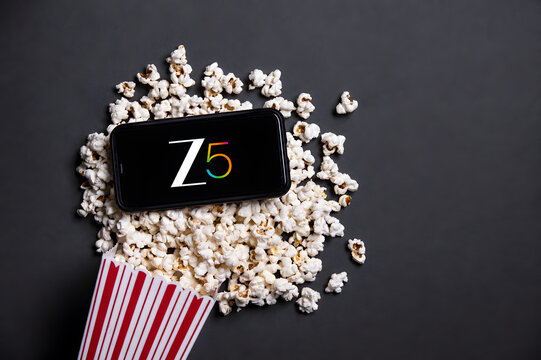 Smartphone showing Z5 OTT streaming app logo on scattered popcorn with striped box on dark background. Indian streaming platform entertainment editorial concept.