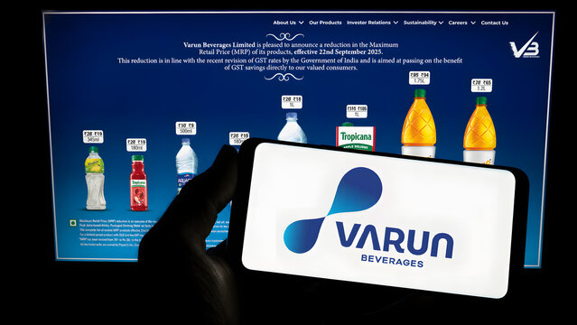 Smartphone showing Varun Beverages logo in front of laptop displaying Pepsi More Fizz website. Indian beverage company PepsiCo bottler digital editorial concept.