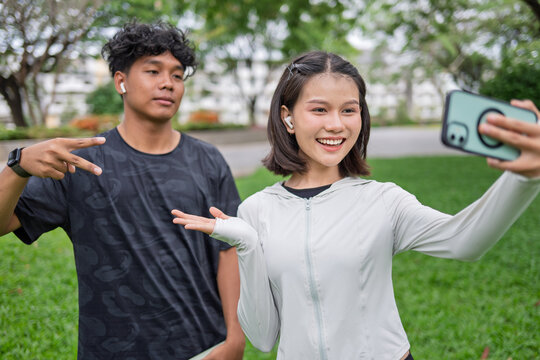 Multicultural Gen Z friends Asian Gen Z woman and African American mixed race man using smartphone taking selfie in green urban park for wellness lifestyle
