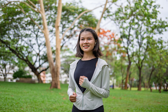 Asian Gen Z woman jogging in green city park for wellness active and feel good lifestyle.