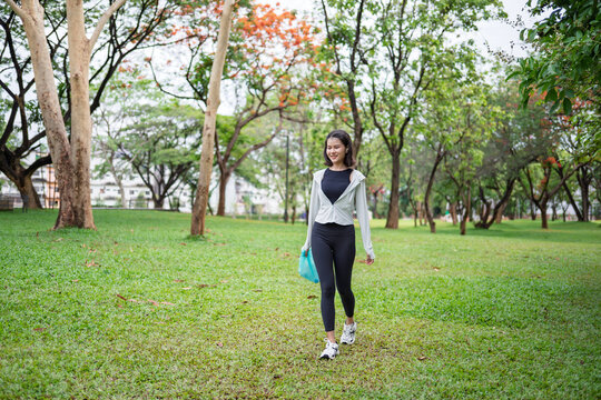 Asian Gen Z woman plogging and collecting trash in green urban park for representing sustainability wellness and positive active lifestyle
