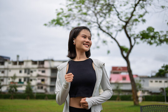 Asian Gen Z woman jogging in green urban park for wellness fitness and active city lifestyle